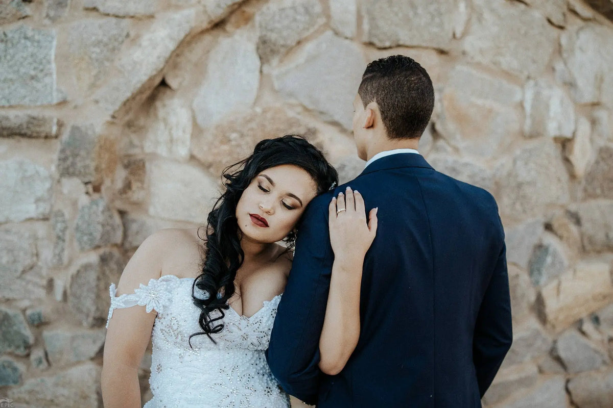 A couple against one of the Courtyard's granite walls at Bezalel Estate, the pale rough-cut stone filling the frame behind them.