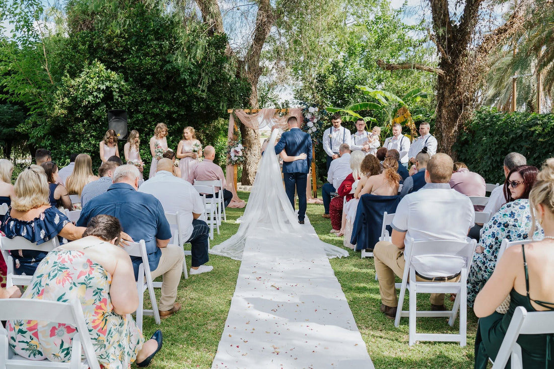 A bridal party walking down a petal-strewn aisle outdoors in spring, guests seated on either side