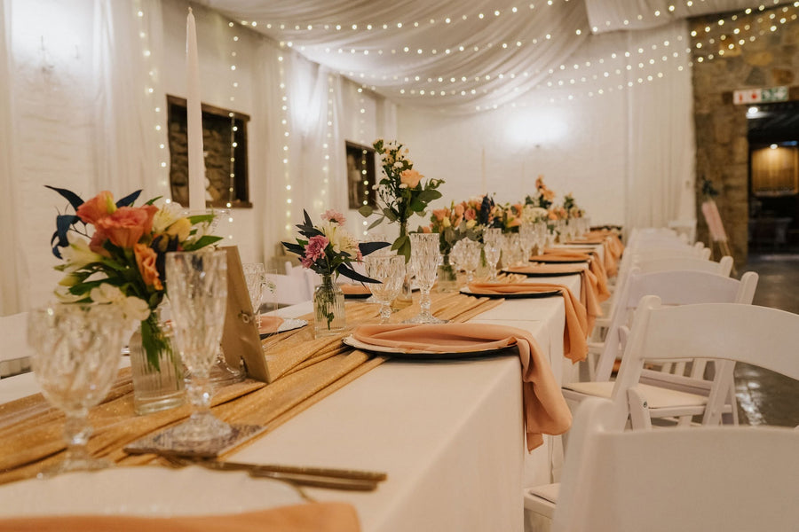 A long reception table laid with pale linen and a floral runner, set under string lights