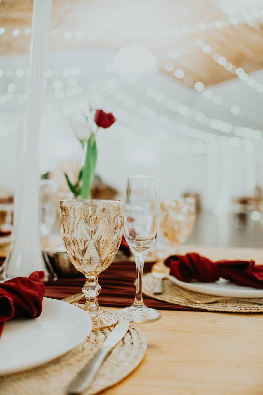 A table set with a red rose and glassware inside the Cellar Hall, strung with fairy lights