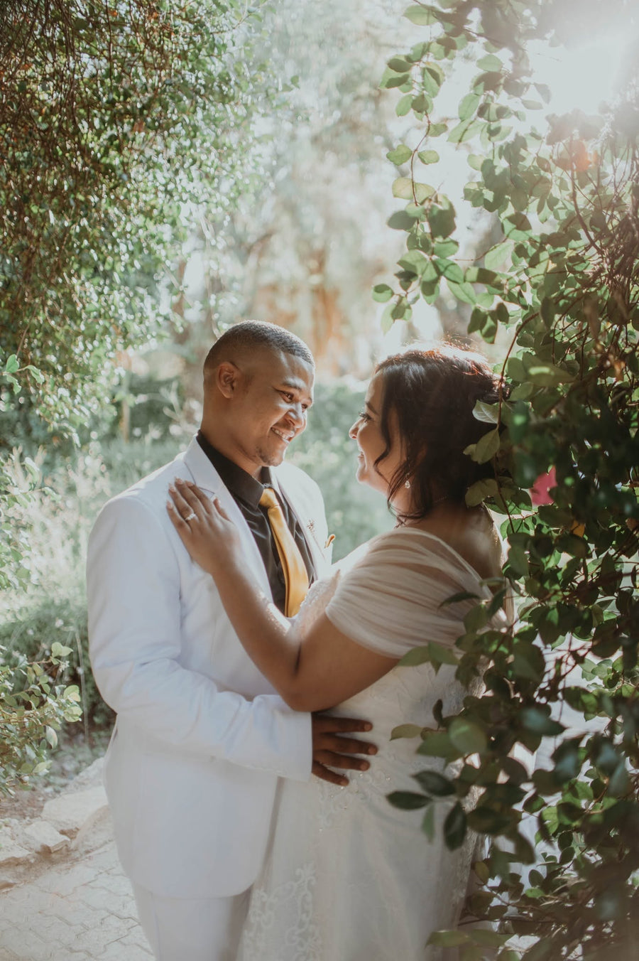 The bride and groom embracing close together, surrounded by garden greenery