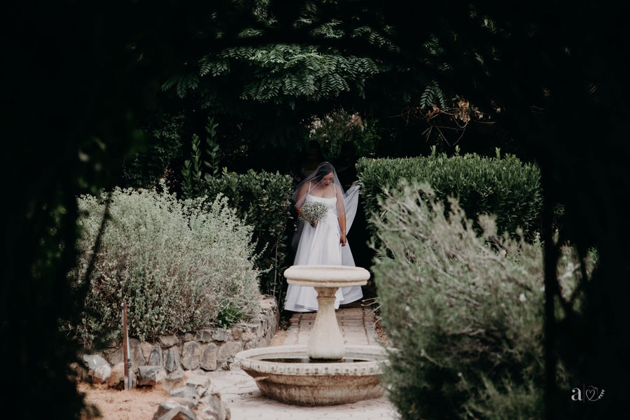 A couple standing together in the garden at dusk, a small stone fountain behind them