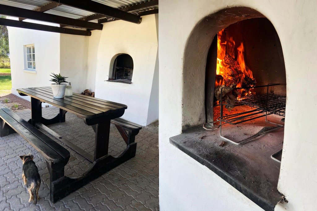 Outdoor setting with a wooden table and benches, and an open fireplace inside a building.