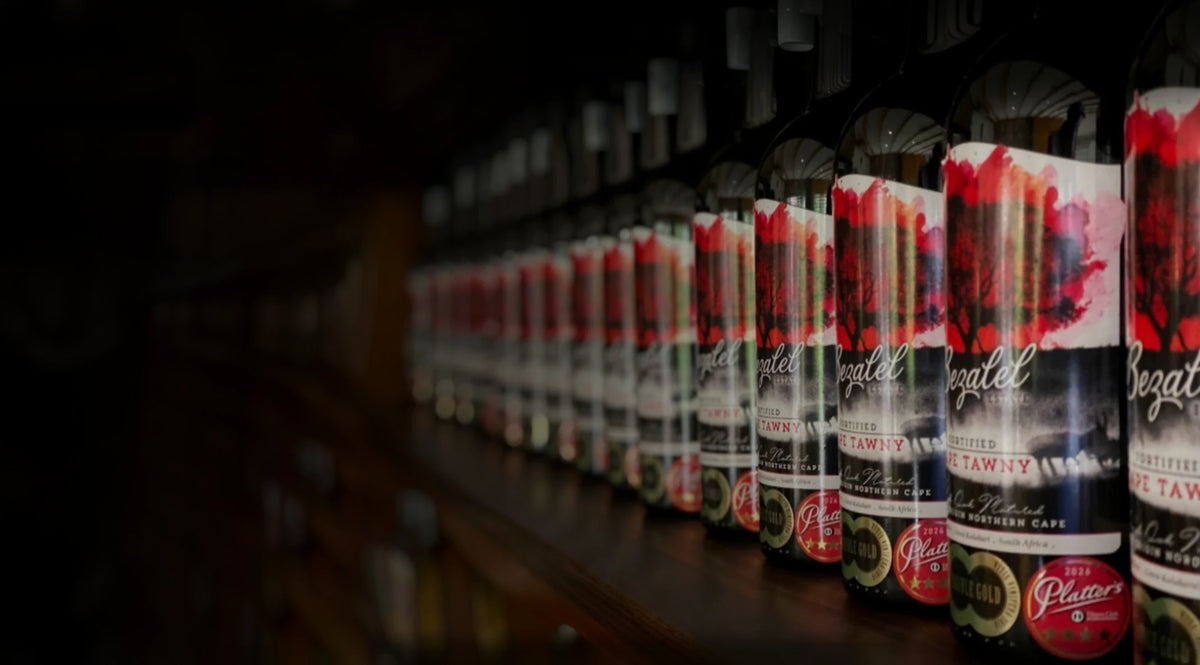 A long row of Bezalel bottles with hand-painted red labels on a dark cellar shelf