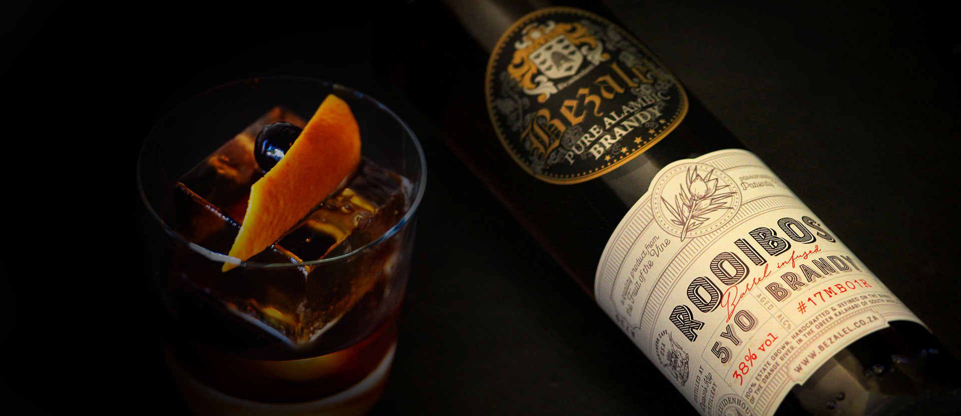 Bottle of Bezalel Rooibos wooden Potstill Brandy with a cocktail garnished with an orange peel on a dark background