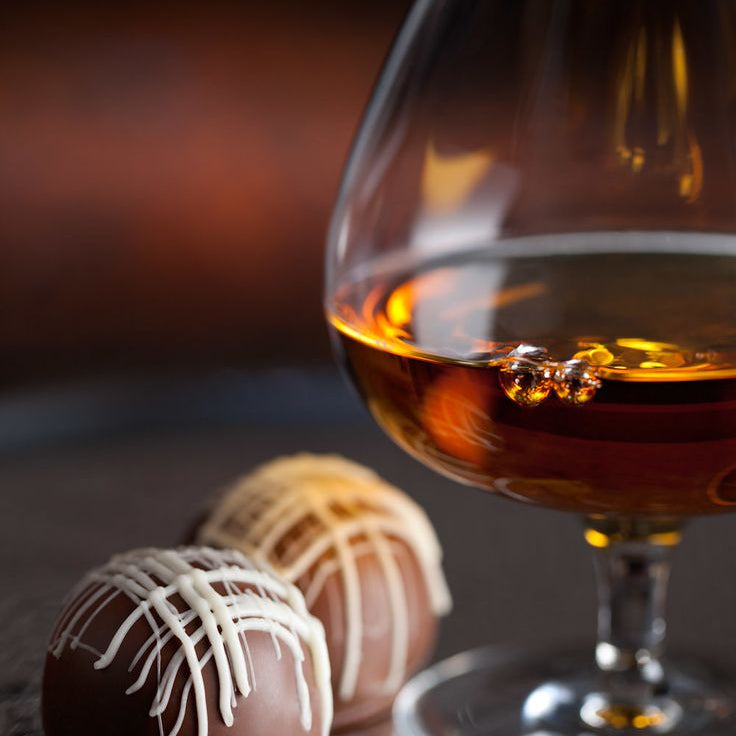 Glass of brandy with two chocolate truffles on a dark surface